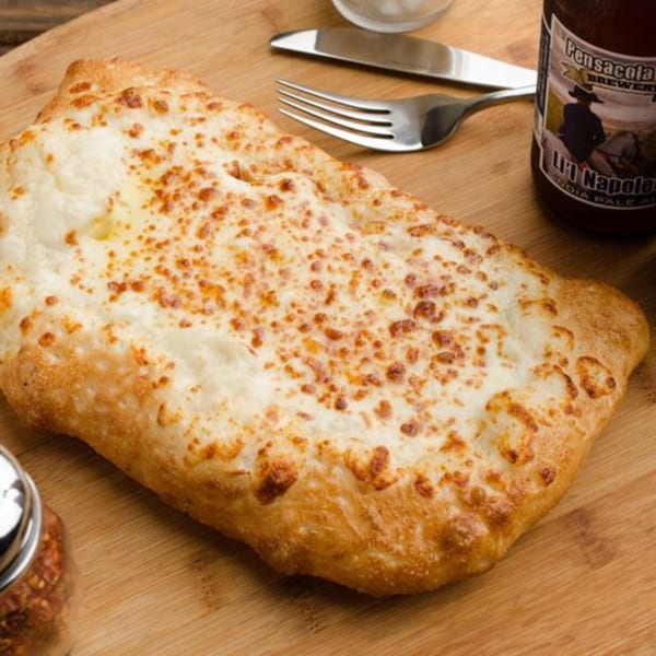 East Hill Pizza's cheesy calzone on a wooden board with a fork, knife, and beer bottle.