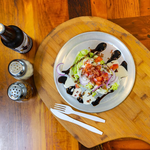 Wedge salad with bacon, tomatoes, red onion, and balsamic glaze on a pizza peel with a beer.