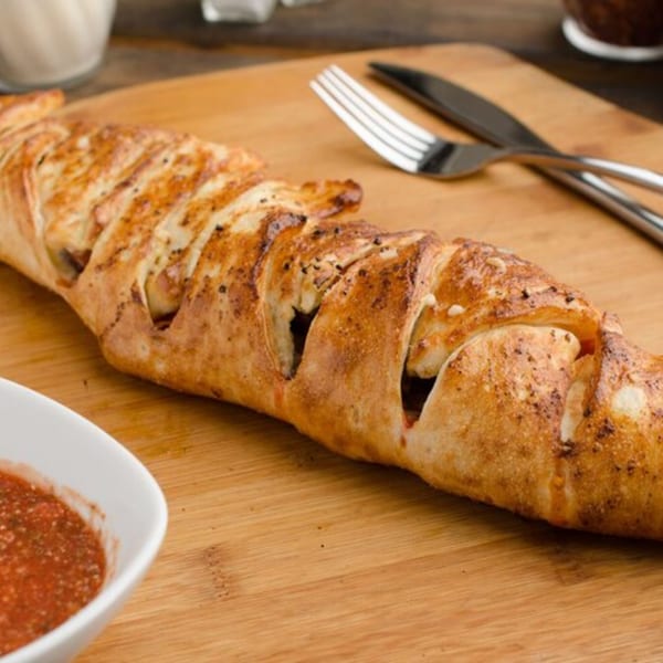 East Hill Pizza's golden-brown stromboli with visible filling, served with marinara sauce on a wooden board.
